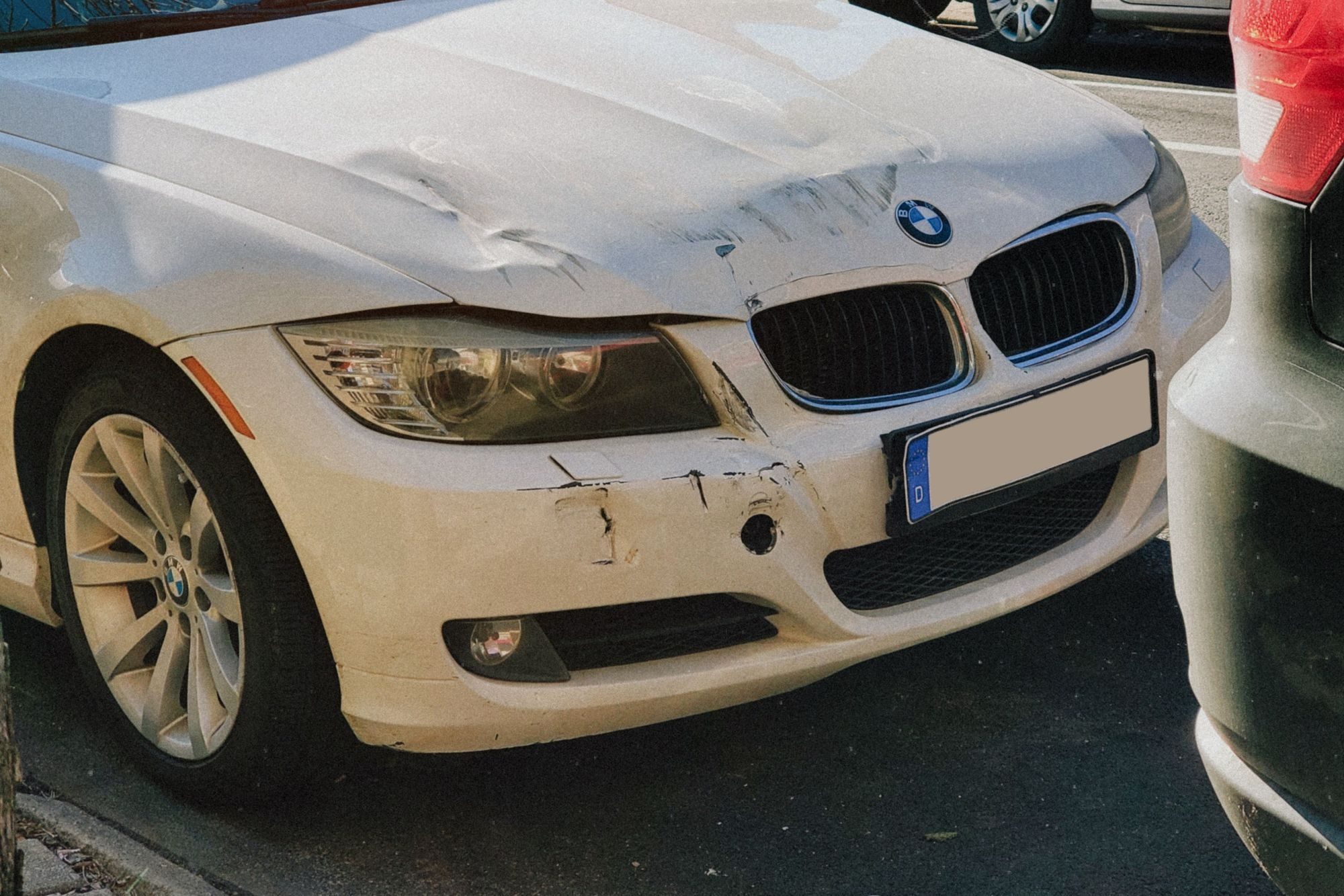 Baltas automobilis su apdaužytu priekiu gatvėje